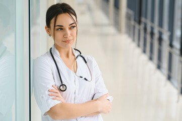 Portrait of young female doctor standing in hospital corridor. Caucasian woman working in nursing home.