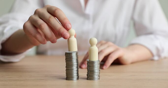Female person in white shirt puts wooden figurines on towers made of coins sitting at desk. Concept of earning money by company members slow motion