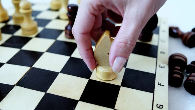 Wood chessboard during game. Knight's move. Female hand making checkmate.