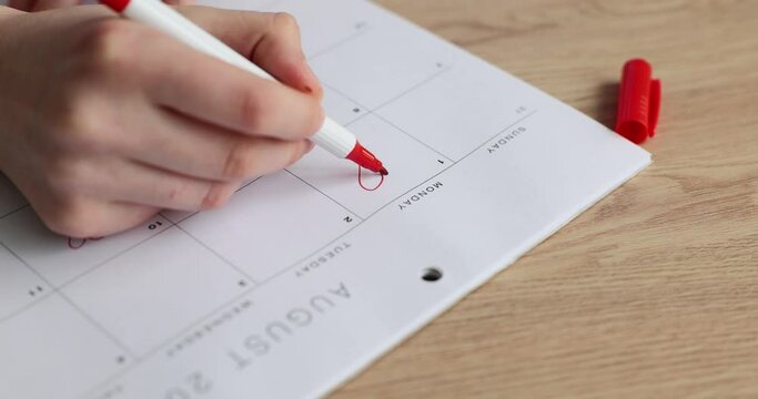Woman hand draws red heart with felt tip pen in daily routine sitting at wooden table. Female person highlighted Monday with love symbol slow motion