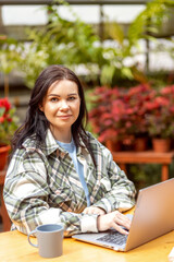 Portrait of a female florist typing on a laptop at a table in a flower shop.