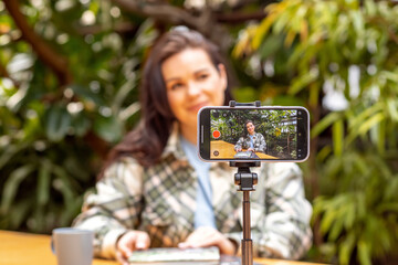 A woman blogger records herself on a smartphone camera standing on a tripod. Freelancer,...