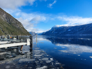 Winter snow in the mountains and melting ice in the Norwgian fjord ferry station Sognefjord