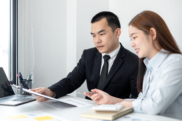 Two business people sitting at workplace and discussing about earnings on a graph to plan investments.