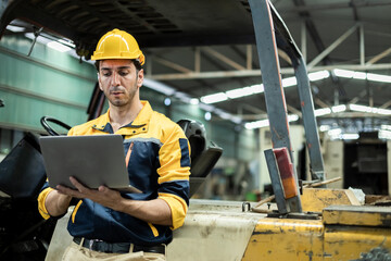 Man engineer wear yellow hard hat and wearing safety uniform standing at forklift using laptop working at heavy industrial factory. manager technician manufacturing. Workers warehouse industrial.