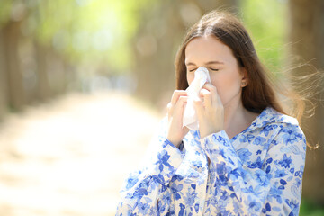 Allergic woman blowing on tissue in a park