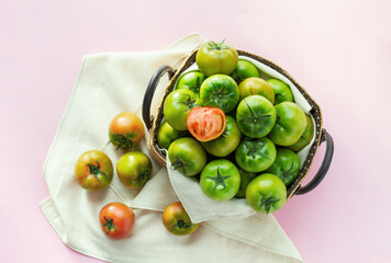 Green salty tomatoes full of a basket on pink background. Top view. 
