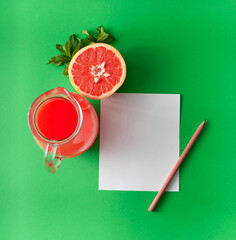 Jug with grapefruit juice with grapefruit slice and mint leaves. and paper card note with pencil on...