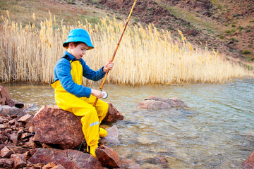 a little fisherman boy with a fishing rod in a yellow fishing jumpsuit