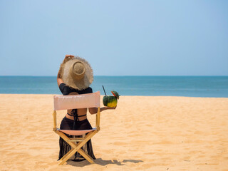 Woman sitting on beach chair with coconut cocktail on the sand. Vacation concept