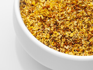 Dried osmanthus flowers in a white bowl on a white background. Close-up, quarter bowl. top and side view. Herbal medicine. Therapeutic tea.