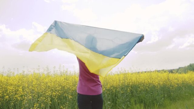 woman with Ukrainian flag in rapeseed field. waving national flag praying for peace. Happy girl celebrating Independence Day.