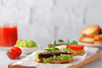 Sandwiches with sprats on toasted slices of bread. Sandwich with smoked sprat - fish, avocado and tomato.
