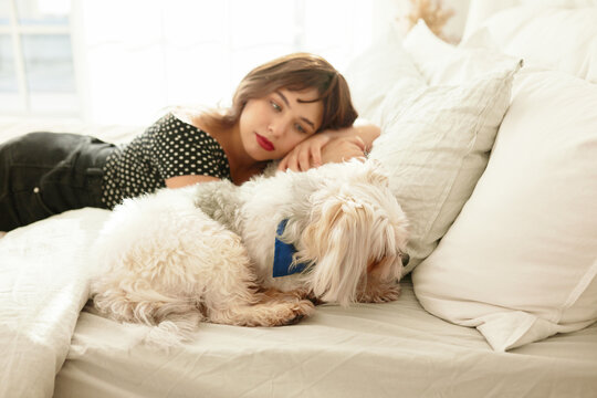 Side view image of pretty young girl and pet lying together comfortably and cuddling in bed, female watching her chinese crested dog sleeping, admiring and protecting its sleep, having rest at home