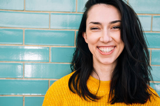 Smiling young woman with black hair in front of brick wall