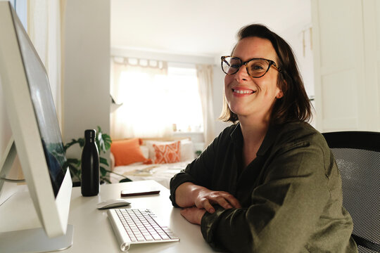 Smiling freelancer with computer at desk in home office