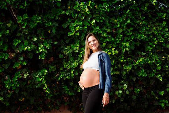 Smiling pregnant woman standing in front of hedge