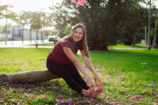 Smiling pregnant woman stretching on log in lawn