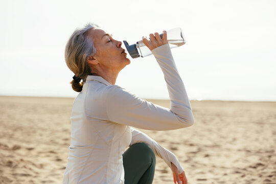 Woman sitting and drinking from water bottle at beach