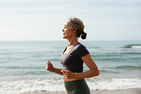 Mature woman with wireless in-ear headphones running at beach