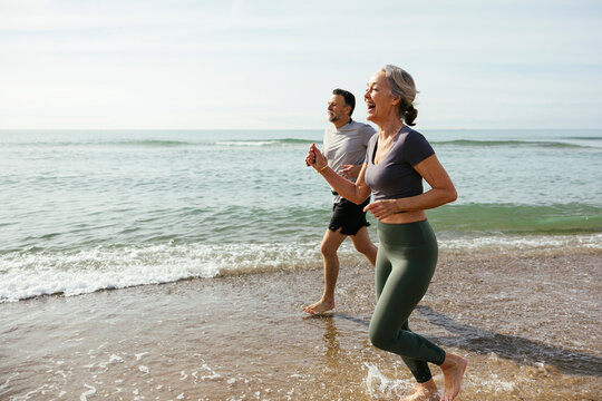 Happy mature couple laughing and running in water at beach