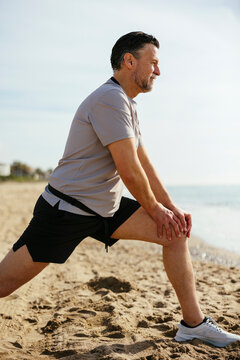 Mature man doing stretching exercise at beach