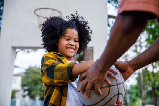 Smiling girl taking basketball form father at sports court