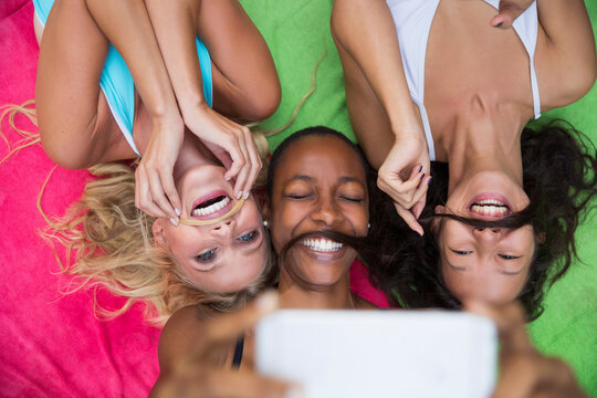 Happy friends imitating mustache lying on colorful blanket