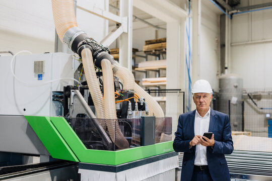 Businessman holding smart phone by modern machine in industry