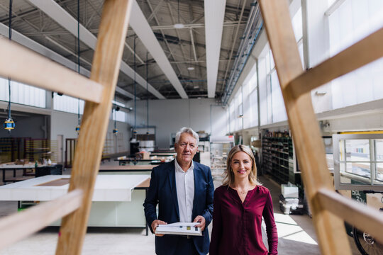 Smiling businesswoman and businessman looking at wooden structure in factory