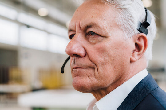 Thoughtful senior businessman wearing headset in factory
