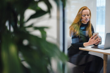 Redhead businesswoman using smart phone sitting in office cubicle
