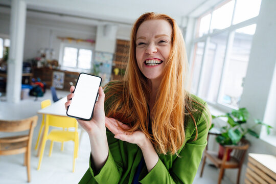 Happy businesswoman showing smart phone screen at office