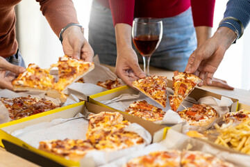 Colleagues having lunch at pizza party and eating assorted pizzas and drinking red wine on rustic wooden table celebrating fast food lunch