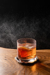 Cocktail with square ice cube and grapefruit slice sprinkled on dark background