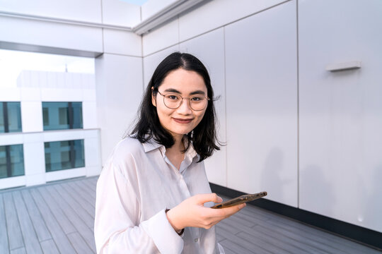 Portrait of young businesswoman with mobile phone on terrace of office building