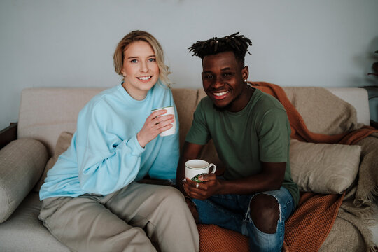 Smiling couple holding coffee mugs sitting on sofa at home