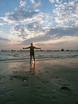 A Person Standing On A Beach With Their Arms Out In The Sunset