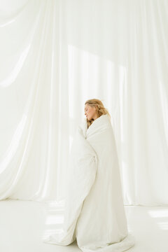 Woman covered in white blanket standing by translucent curtain