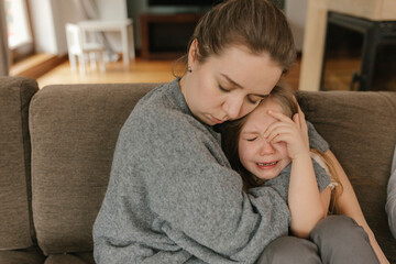 Mother consoling crying daughter on sofa
