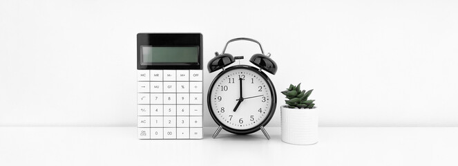 Black alarm clock with calculator against a white wall. Financial concept.