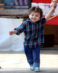 Cute little toddler boy with great happy and smile walking on the street of a village and holding hand of mother. Wearing blue denim and shirt. Portrait in a bright sunny day