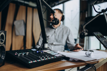 Obraz na płótnie Canvas Smiling and gesturing radio host with headphones on his head reading news from paper into studio microphone on radio station.