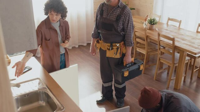 High angle shot of Caucasian woman telling professional plumbers about breakage of faucet