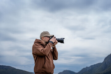 Young adult male traveler taking photo using camera with mountains view