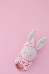 Baby rattle toy. Children's knitted rabbit on a pink background for a girl. Handmade rattle for a newborn.