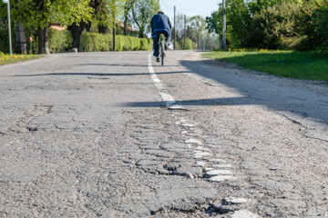 Damaged asphalt road. A cyclist in the background