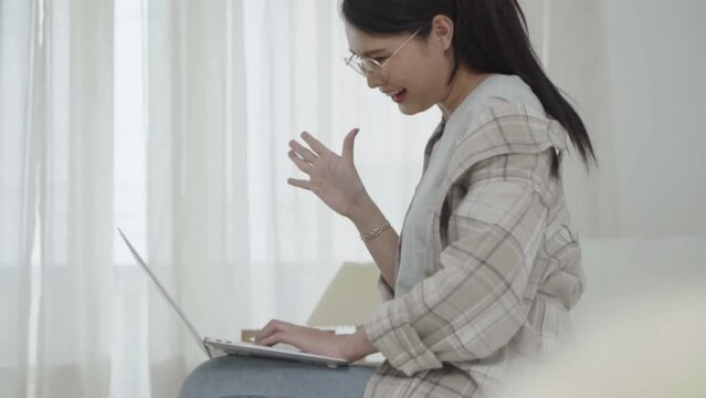 Asian freelance business woman using laptop 
 video call  freind in bed at home.