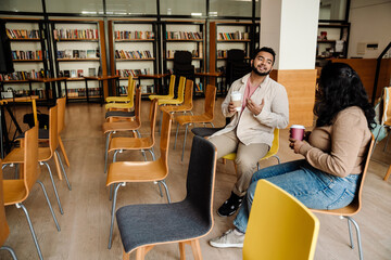 Fototapeta premium Indian man talking with ?ollege classmate and drinking coffee while sitting in library
