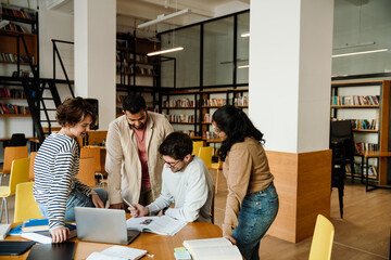 Group of young students working on university project together in library